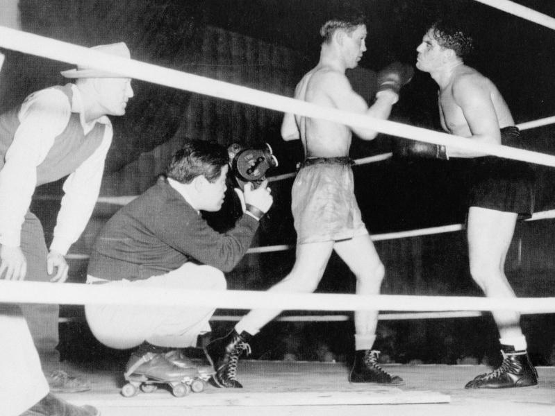 James Wong Howe on roller skates in a boxing ring, he squats down to get a shot of the two boxers
