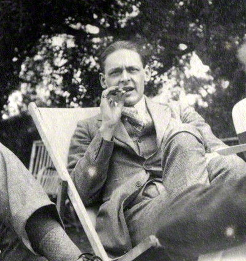 T. S. Eliot is shown seated outside and smoking a cigarette. T. S. Eliot is shown seated outside and smoking a cigarette.